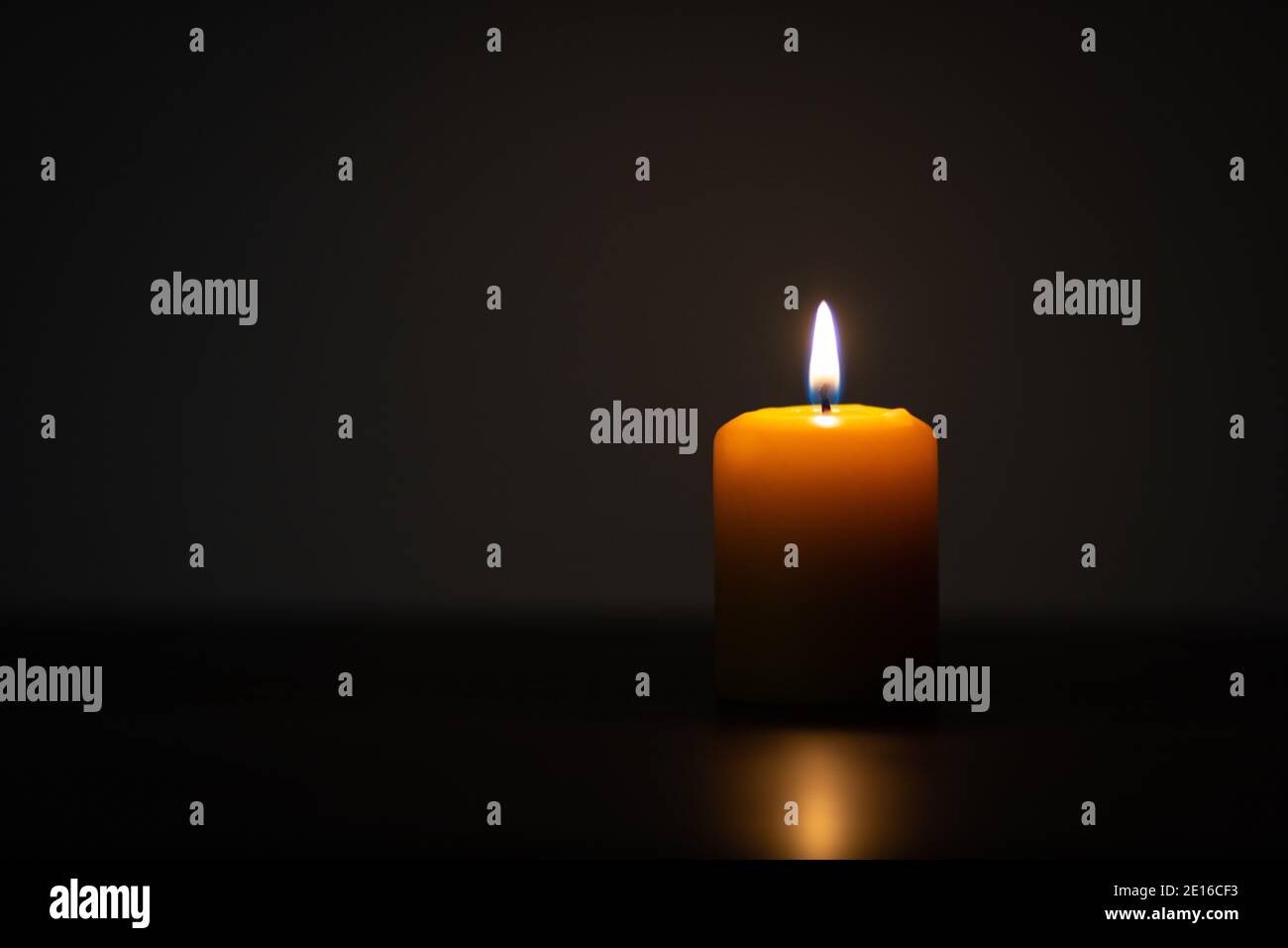 Candela gialla che brucia su sfondo scuro e posto fuori centro. Impostazione minimalista con spazio vuoto per il testo a sinistra Foto Stock