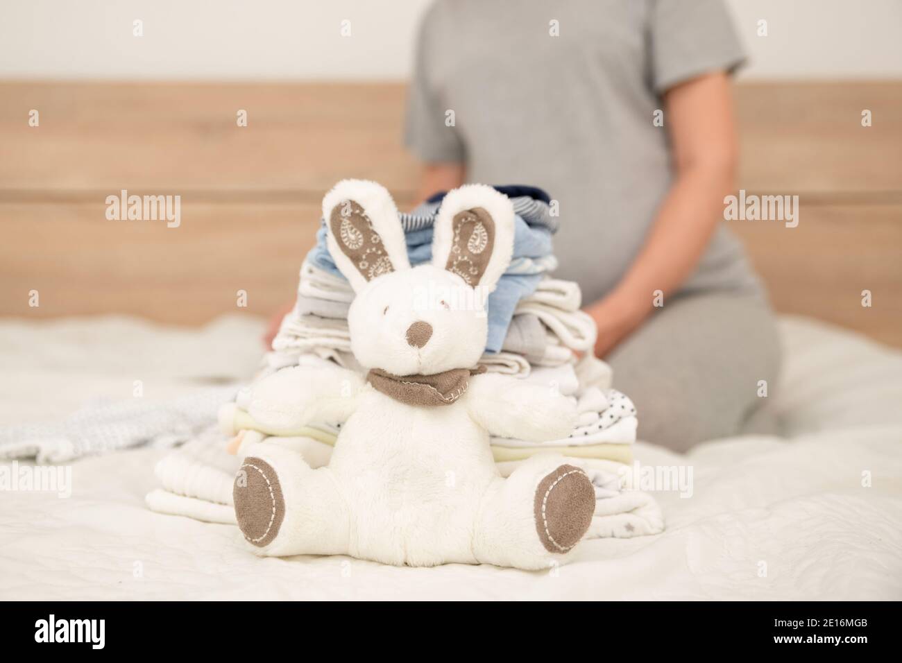 Mucchio di vestiti del bambino, coniglio e donna incinta su un letto Foto Stock