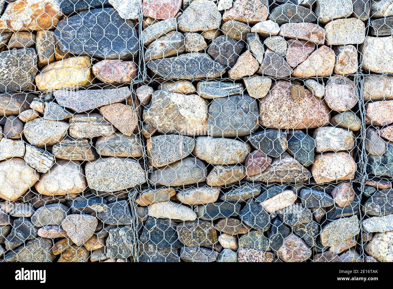 Muro di pietra con griglia metallica come sfondo. Struttura rock in griglia metallica. Rete Gabion Foto Stock