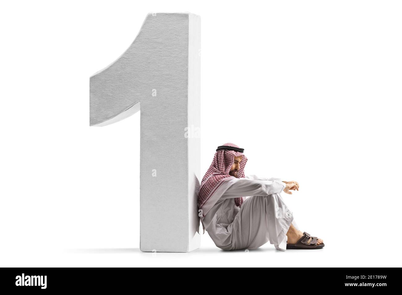 Uomo arabo saudita pensivo seduto sul pavimento e appoggiato su un numero uno isolato su sfondo bianco Foto Stock