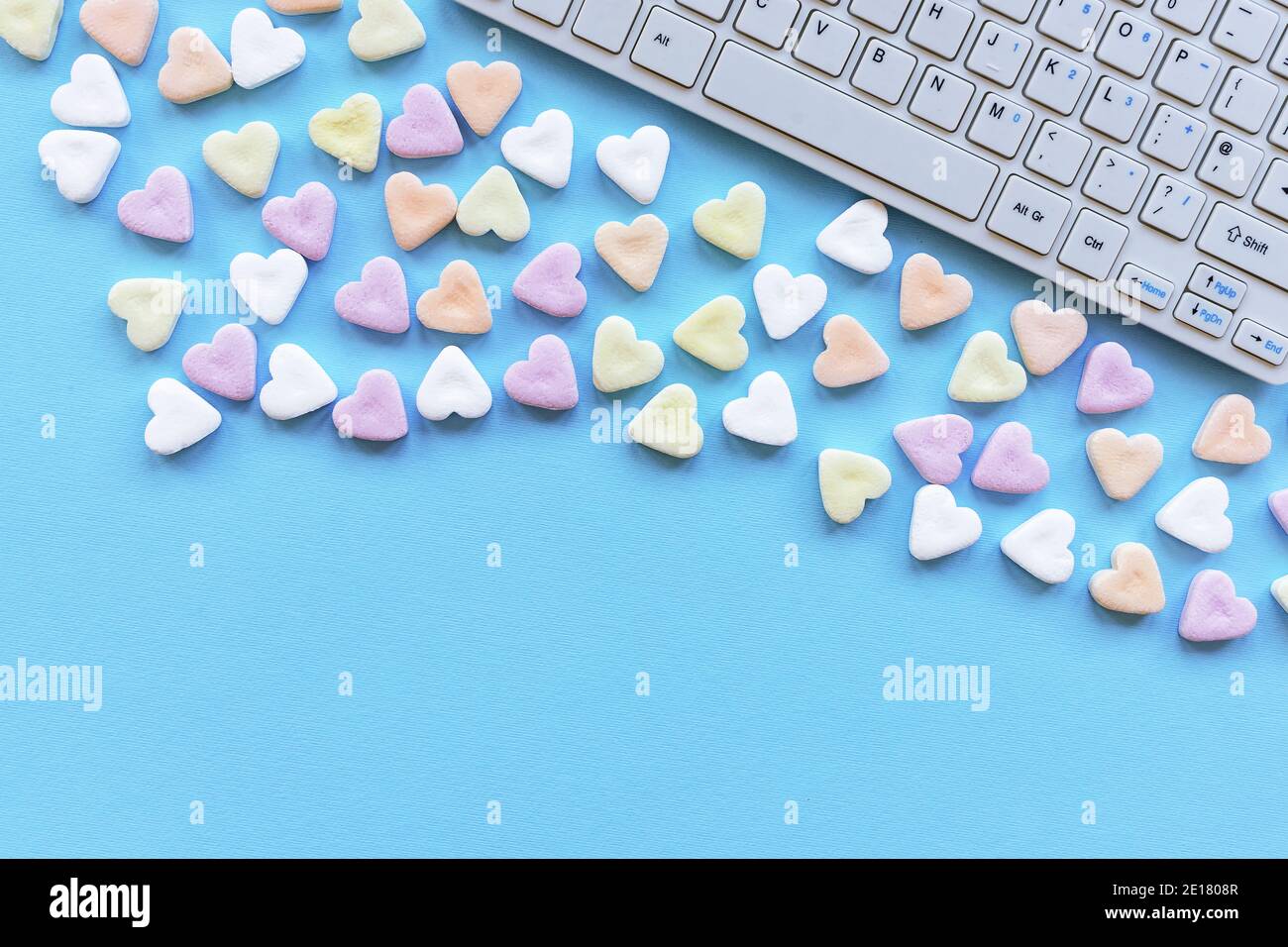 Caramelle a forma di cuore e tastiera computer su un tavolo blu. Concetto di San Valentino. Vista dall'alto, disposizione piatta, spazio per la copia. Foto Stock