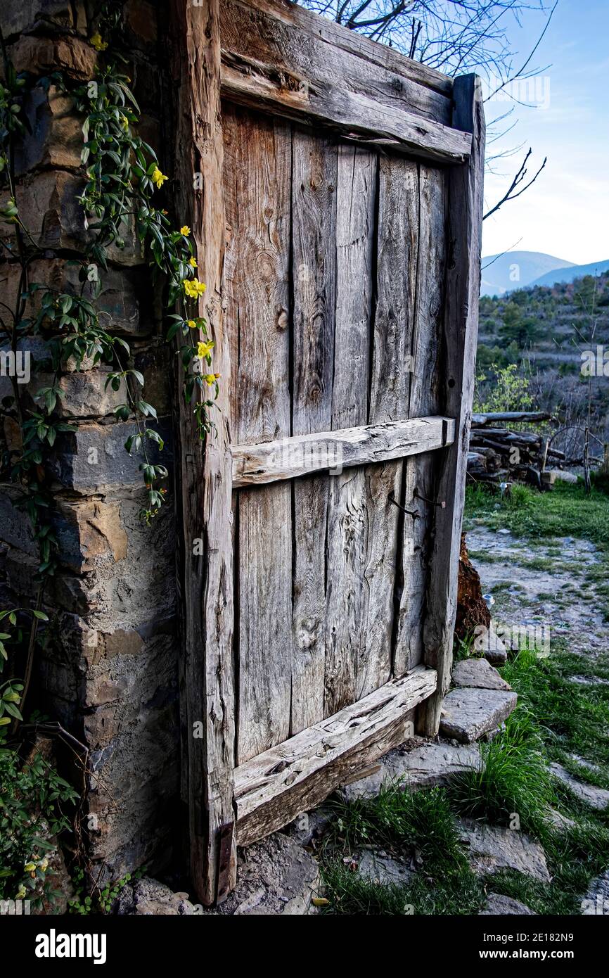 vecchia porta di legno parzialmente aperta da una casa di villaggio con piccoli fiori gialli su un lato e una vista di la campagna sullo sfondo Foto Stock