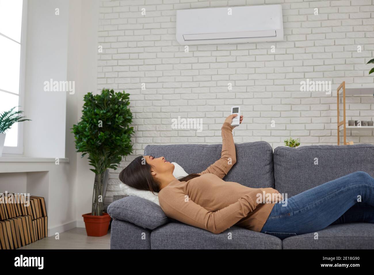 Donna sdraiata sul divano a casa e che si accende l'aria condizionatore con  telecomando Foto stock - Alamy