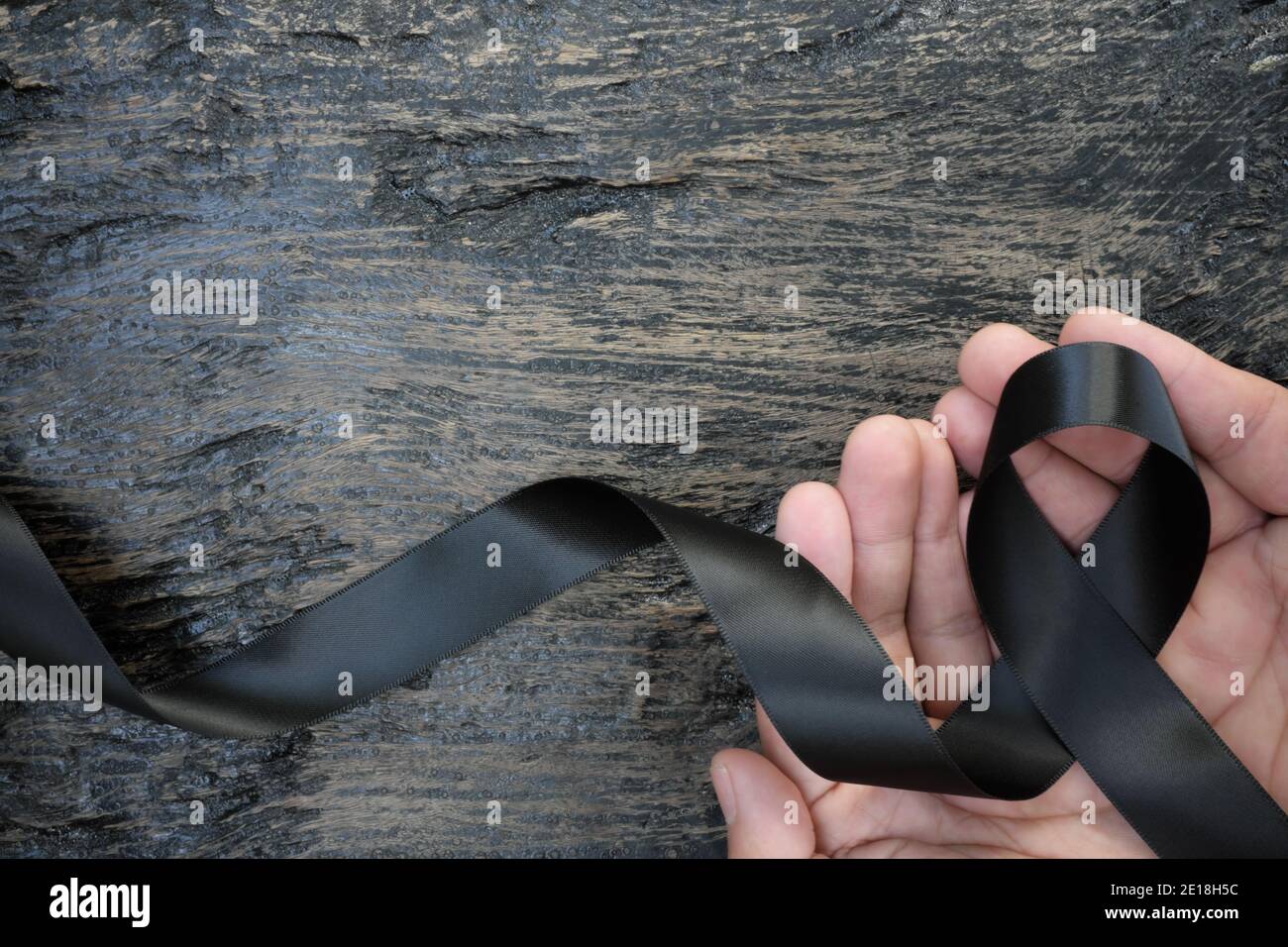 Vista dall'alto della mano maschio che tiene il nastro nero su sfondo di legno scuro con spazio di copia. Melanoma o cancro della pelle, prevenzione delle bande e consapevolezza della narcolessia Foto Stock