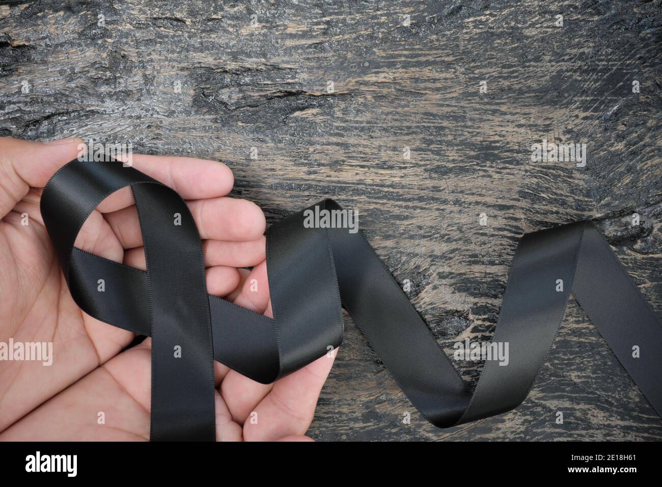 Vista dall'alto della mano maschio che tiene il nastro nero su sfondo di legno scuro con spazio di copia. Melanoma o cancro della pelle, prevenzione delle bande e consapevolezza della narcolessia Foto Stock