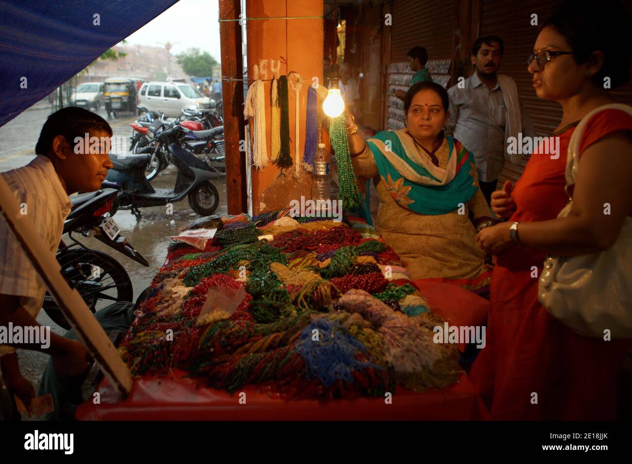 Donne che negoziano con un venditore di gioielli di collana ad un mercato stradale durante una giornata piovosa a Jaipur, Rajasthan, India. Foto Stock