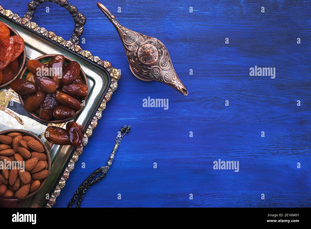 Lampada Aladdin, perle di preghiera e vassoio egiziano con noci, datteri, albicocche secche su tavolo di legno blu. Cibo sano per rompere veloce in Ramadan. Piatto la Foto Stock