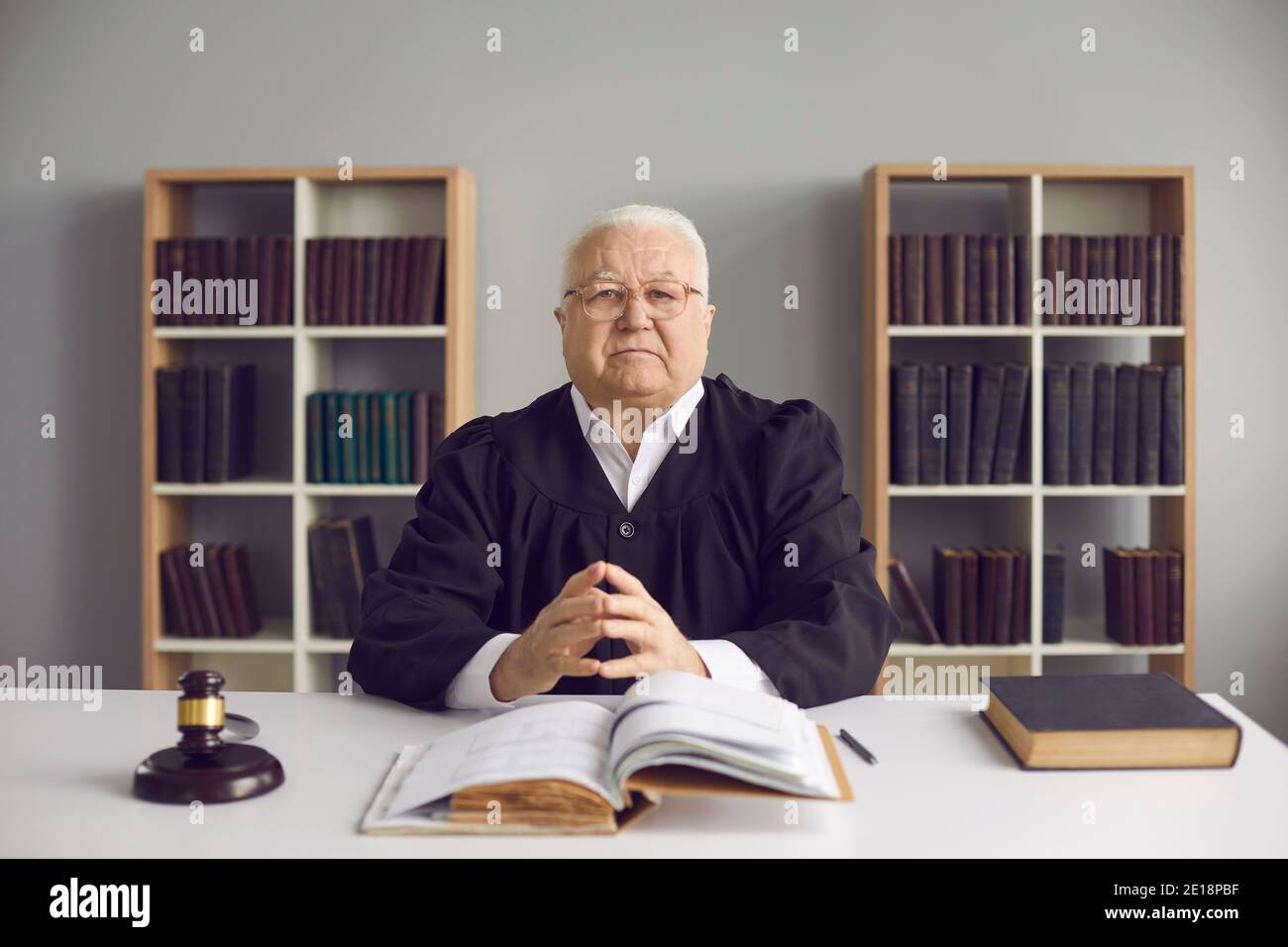 Saggio giudice maturo seduto alla scrivania con codice aperto di Legge nel suo ufficio o in aula Foto Stock