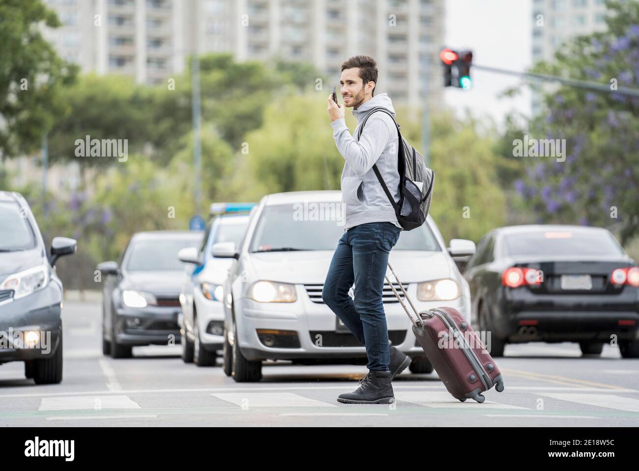 Giovane uomo con bagagli che attraversano la strada Foto Stock