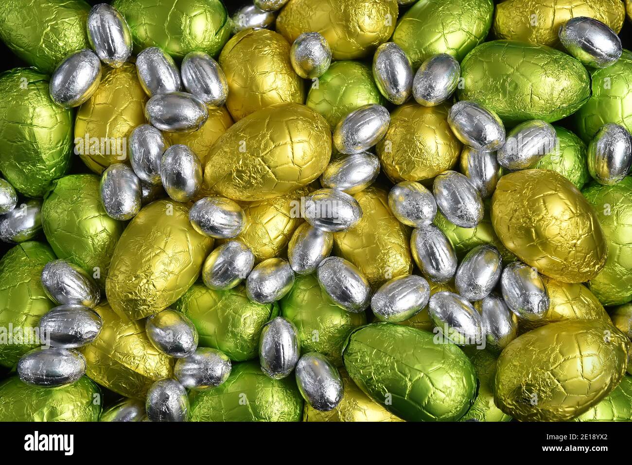 Grandi e piccoli colori giallo, oro, verde, verde calce e argento primavera di cioccolato avvolto foglia uova di pasqua, su uno sfondo nero. Foto Stock