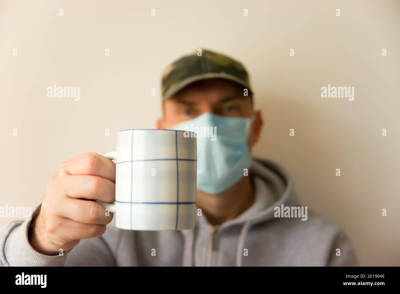 Un uomo in una maschera chirurgica che tiene una tazza Foto Stock