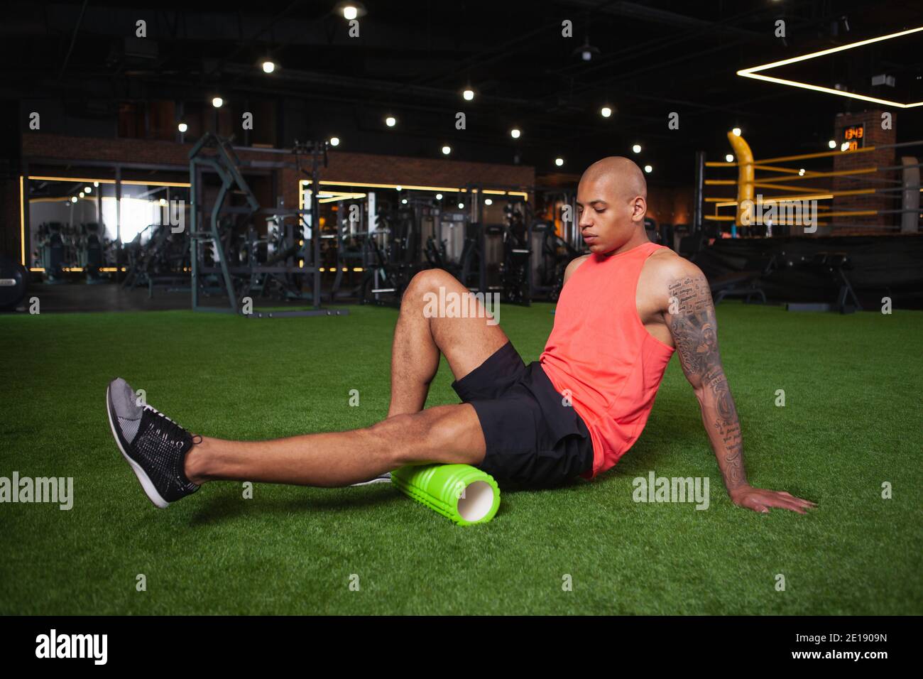 Attraente giovane atleta africano maschile rilassante muscoli delle gambe dopo l'allenamento in palestra, utilizzando il rullo in schiuma. Atletico bell'uomo che riposa dopo l'esercizio fisico, utilizzando Foto Stock