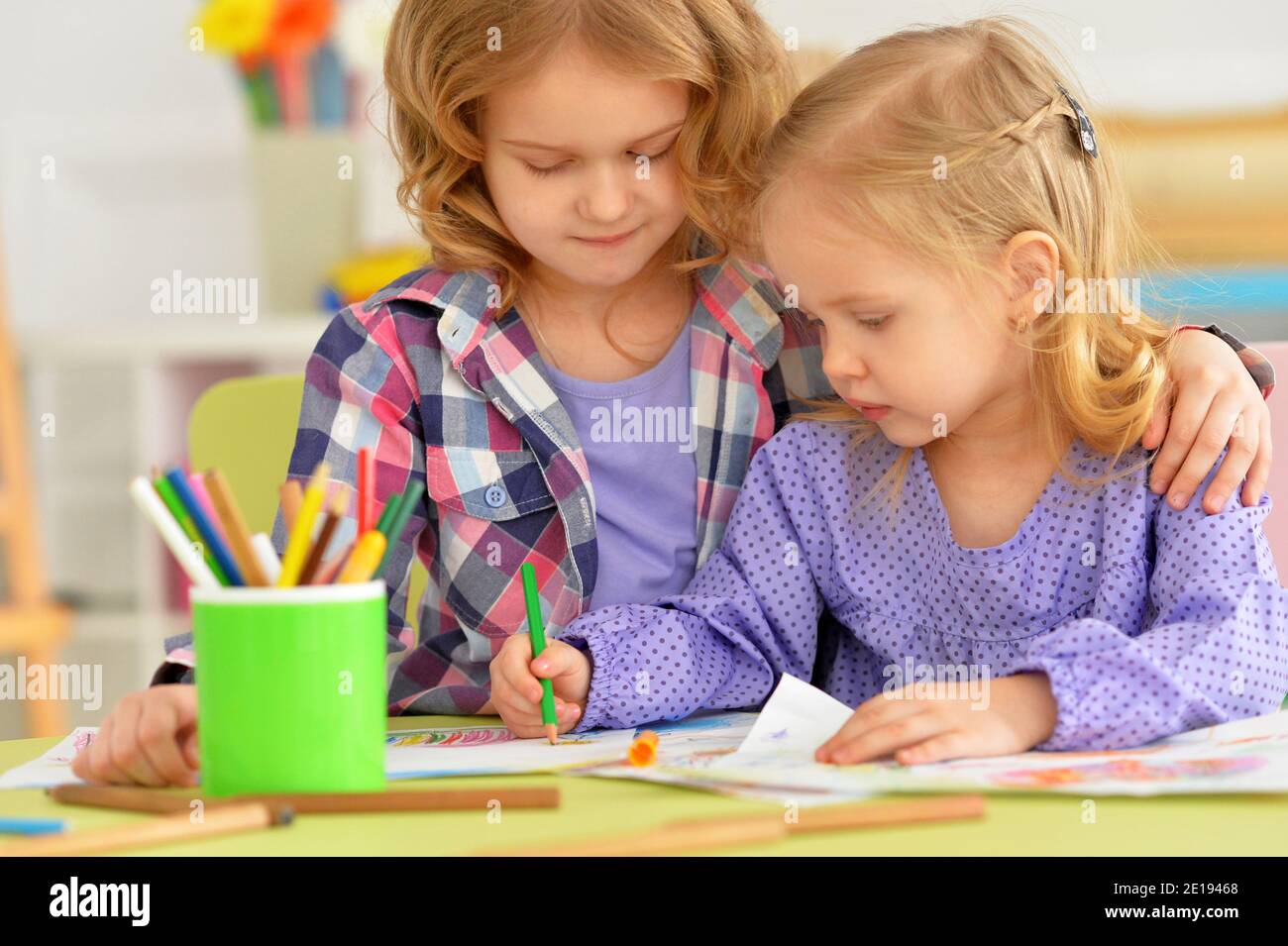 Carino ragazze piccole che si siedono a tavola e disegno Foto Stock