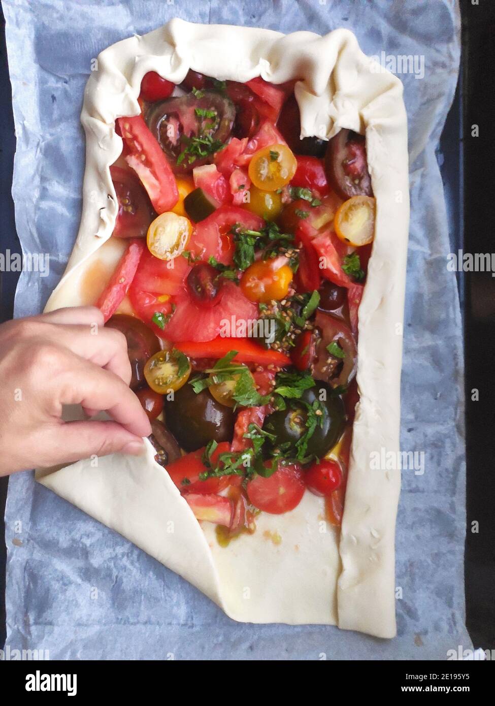 Una mano umana che prepara pizza fatta in casa con pomodori freschi e alcune foglie di frasino di basilico. Foto Stock