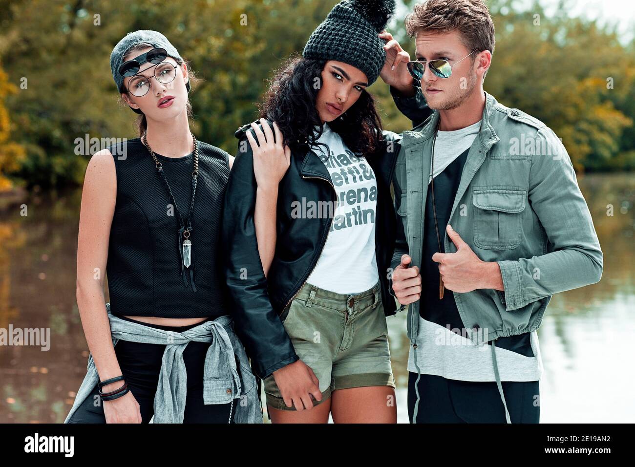 Ritratto di 3 giovani adulti che si levano a stretto contatto di fronte ad un lago in un parco naturale durante una giornata di sole in primavera indossando abiti urbani freschi. Foto Stock
