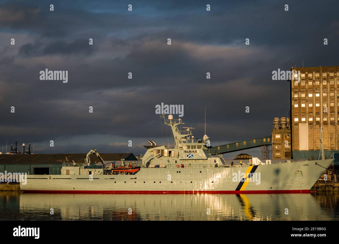 MPV Jura, nave di protezione marina per la pesca del governo scozzese e silo di grano industriale con riflessi, Imperial Dock, Leith, Edimburgo, Scozia, Regno Unito Foto Stock