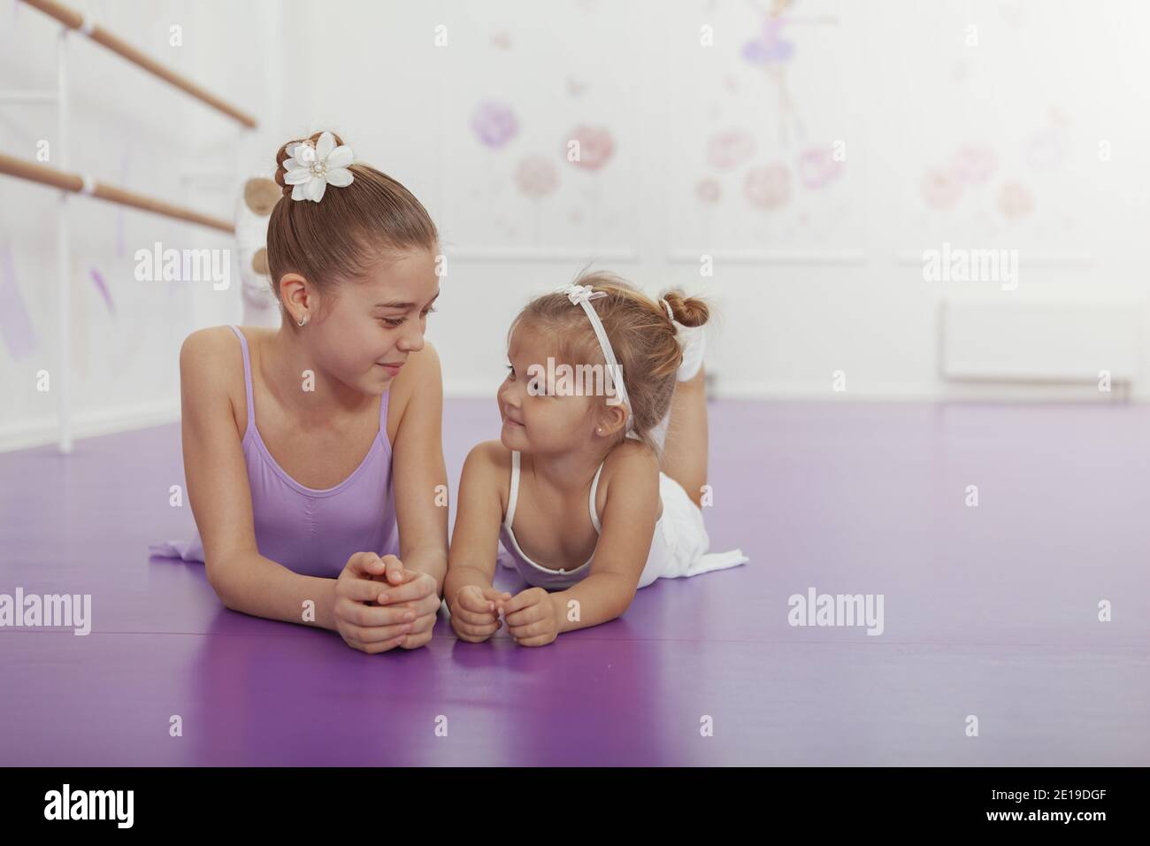 Adorabili ballerine in leotards e tutu gonne che riposano alla scuola di balletto dopo l'esercizio. Ballerine Sistars sorridenti l'una all'altra, sdraiati sulla t Foto Stock