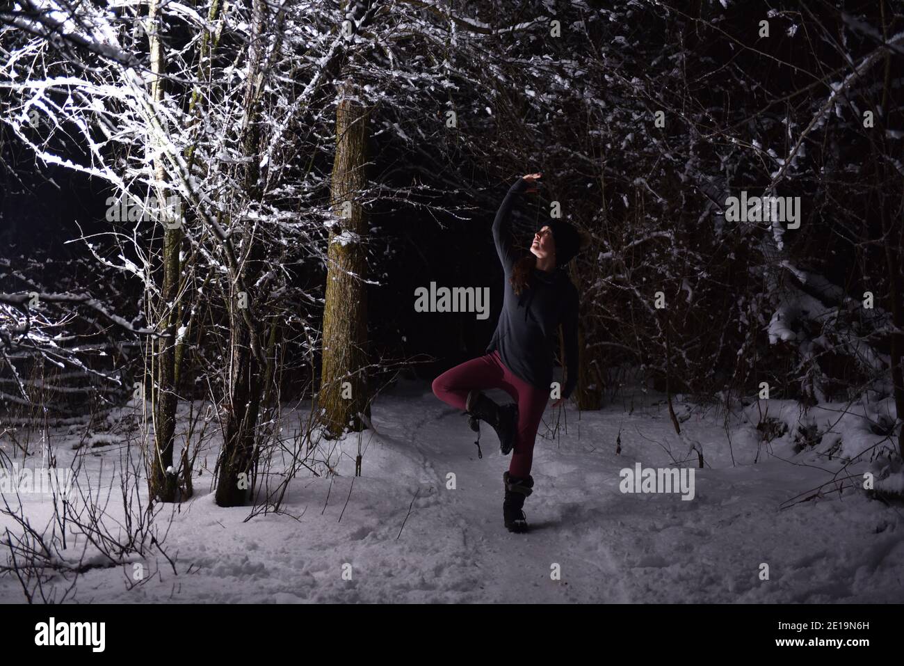 Praticare yoga in inverno, nella foresta di notte nella neve. Nuove sfide con neve e freddo vi insegnano come raggiungere la messa a fuoco e il controllo. Foto Stock