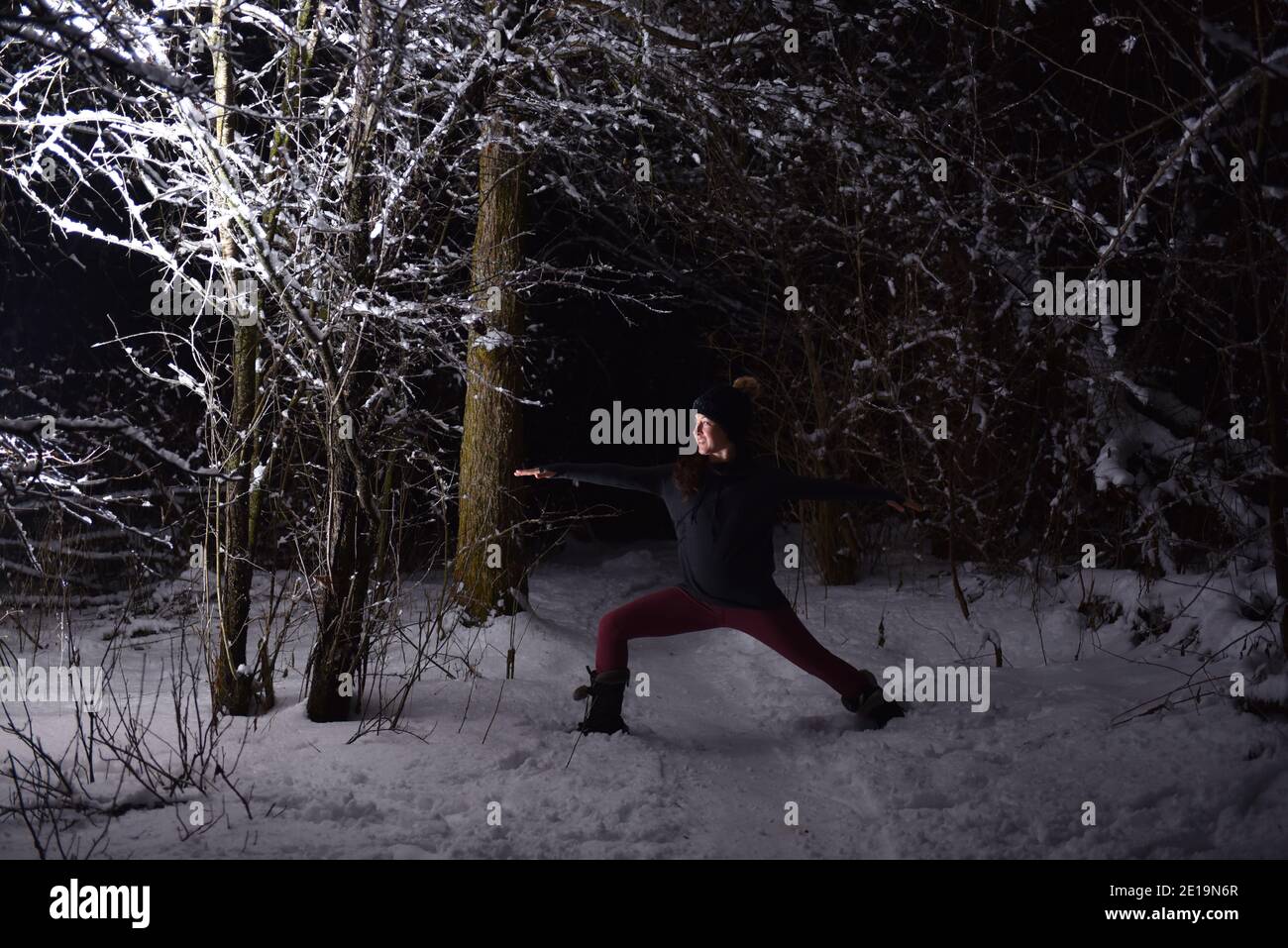 Praticare yoga in inverno, nella foresta di notte nella neve. Nuove sfide con neve e freddo vi insegnano come raggiungere la messa a fuoco e il controllo. Foto Stock