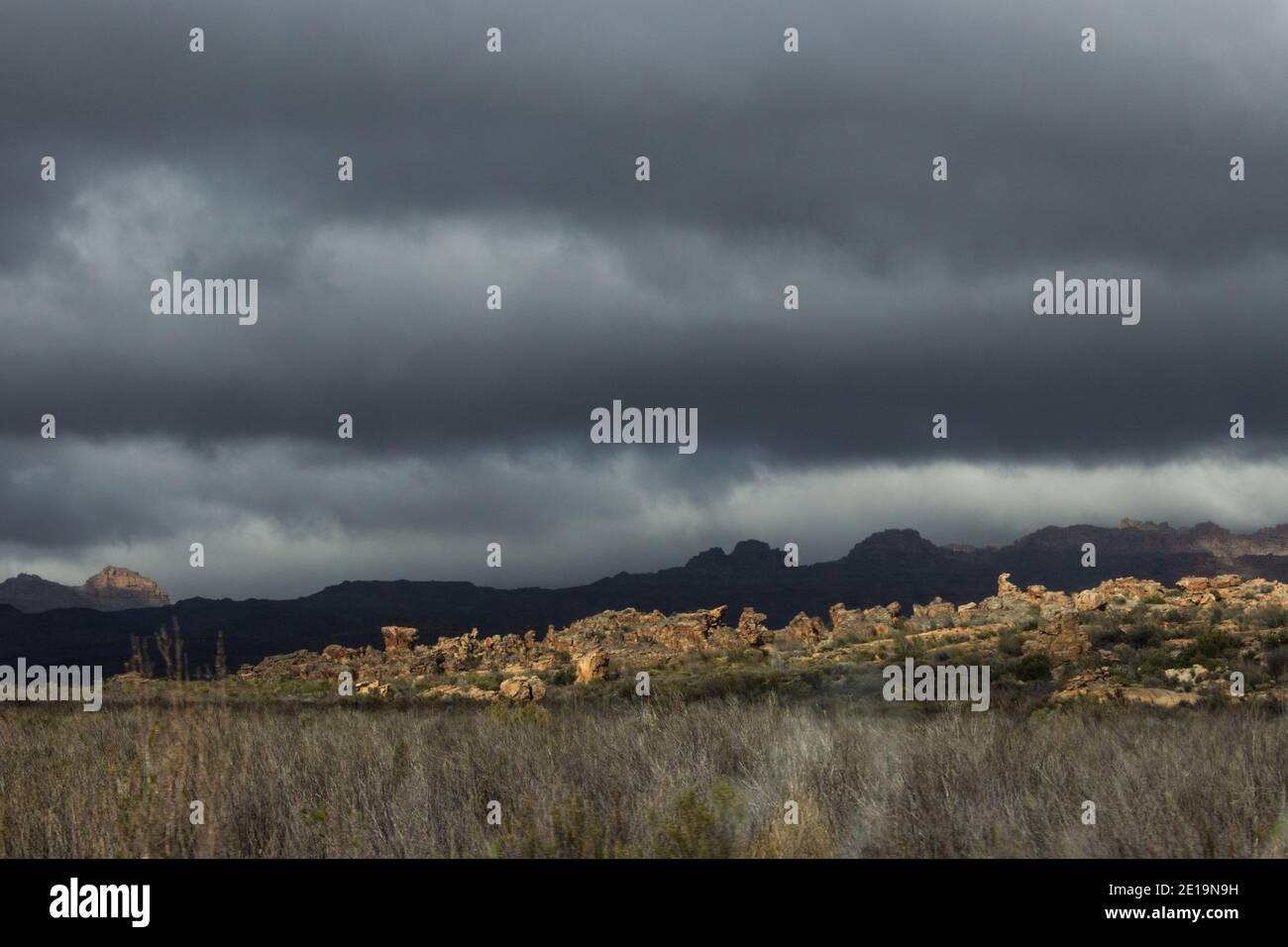 Un cielo oscuro e tempestoso sulla catena montuosa ombreggiata di Cederberg, con una cresta esposta di massi di arenaria in primo piano Foto Stock