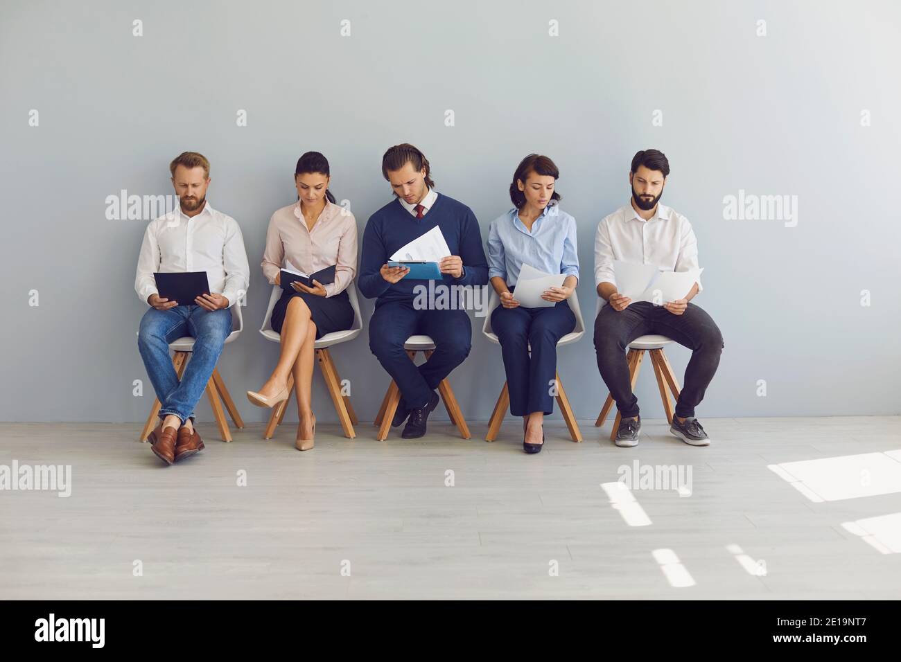 Gruppo di cercatori di lavoro seduti su sedie in fila con riprende e attende in linea per il colloquio Foto Stock
