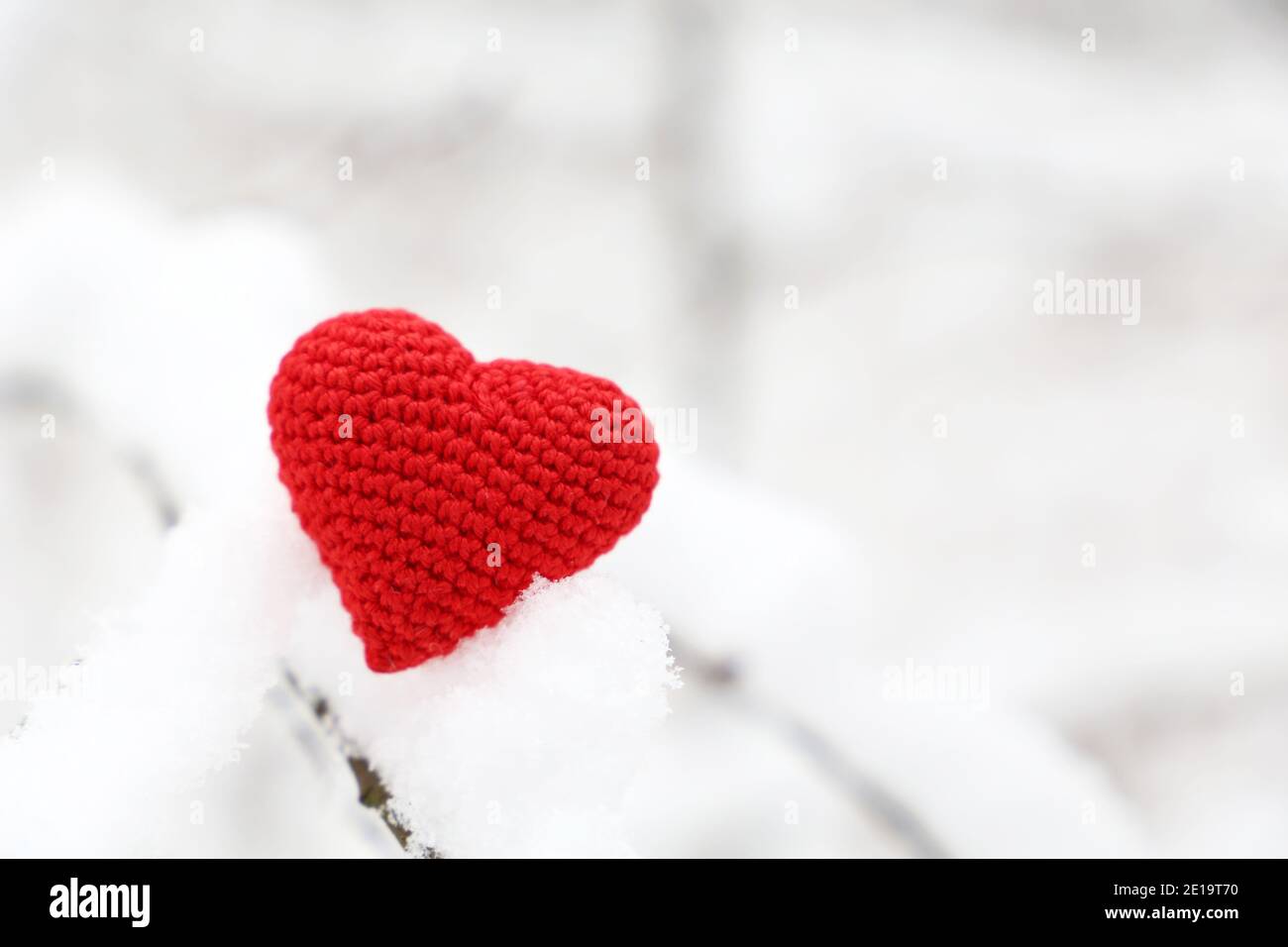 Cuore di San Valentino nella foresta invernale, clima freddo. Cuore rosso lavorato a maglia su ramo innevato, simbolo di amore romantico, sfondo per le vacanze Foto Stock