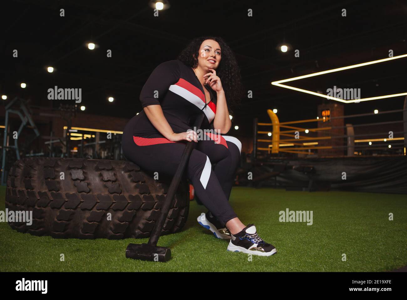 Tiro ad angolo basso di una donna di taglia Plus in abbigliamento sportivo riposante in palestra dopo aver fatto esercizio con il martello. Allegro sportivo sovrappeso rilassante afte Foto Stock