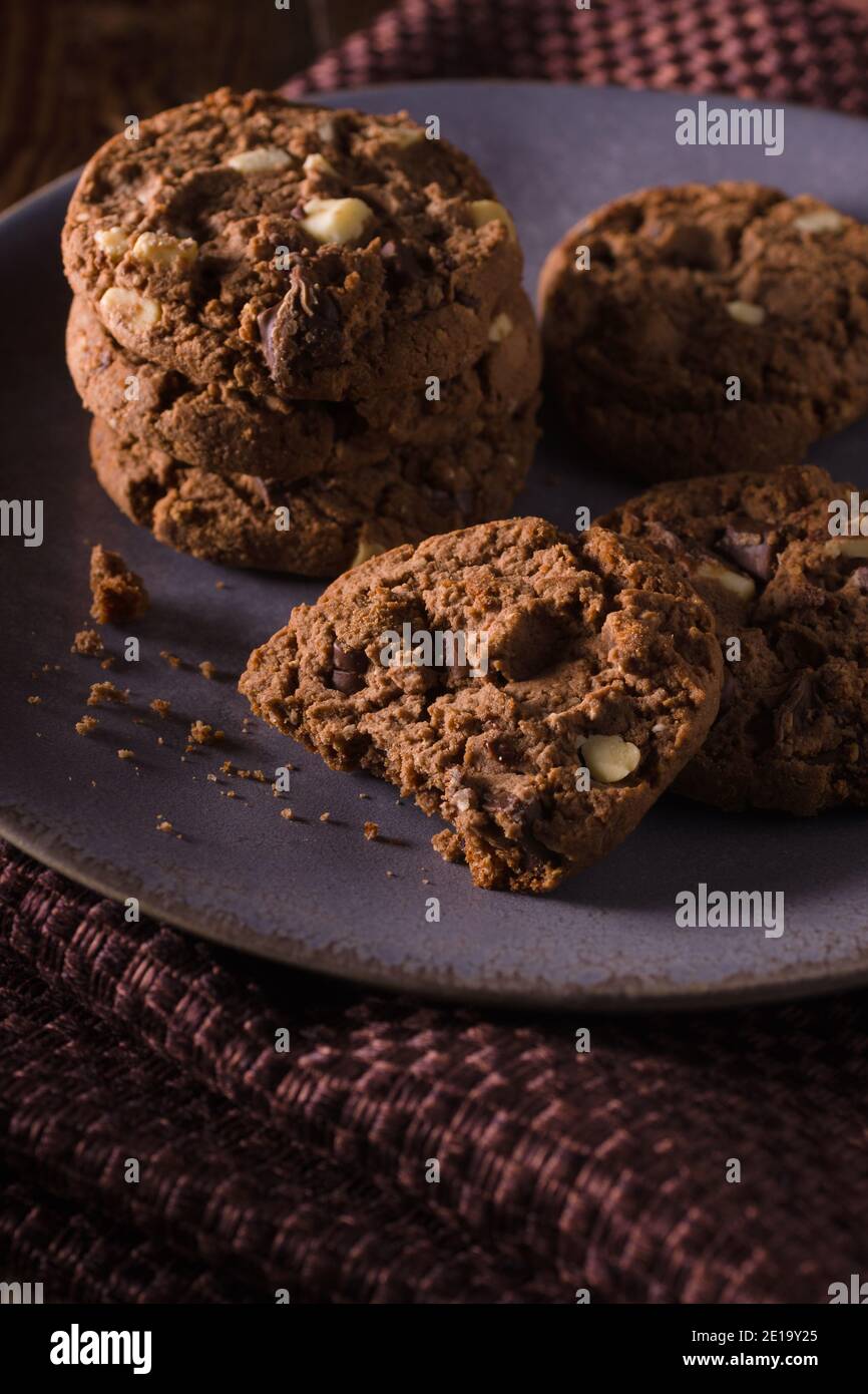 Triplice biscotti al cioccolato con pezzi di latte bianco e. cioccolato fondente con illuminazione creativa scura Foto Stock