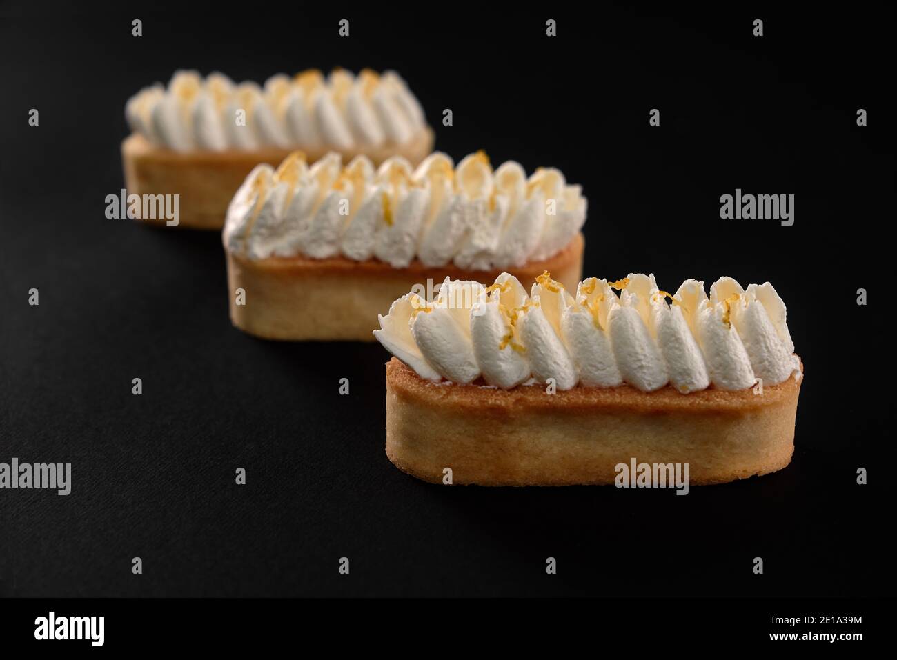 Fuoco selettivo di biscotti lunghi del biscotto con la parte superiore montata del mascarpone della crema. Tre dolci freschi fatti in casa isolati su sfondo nero. Concetto di dolci, industria alimentare. Foto Stock