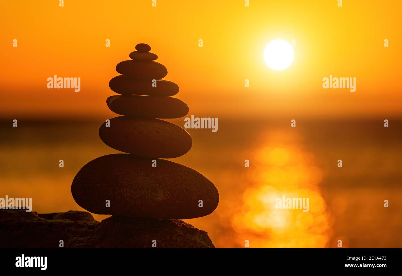 Profilo a piramide di ciottoli bilanciato sulla spiaggia. Astratto caldo tramonto bokeh con Mare sullo sfondo. Pietre Zen sulla spiaggia di mare, meditazione, spa Foto Stock