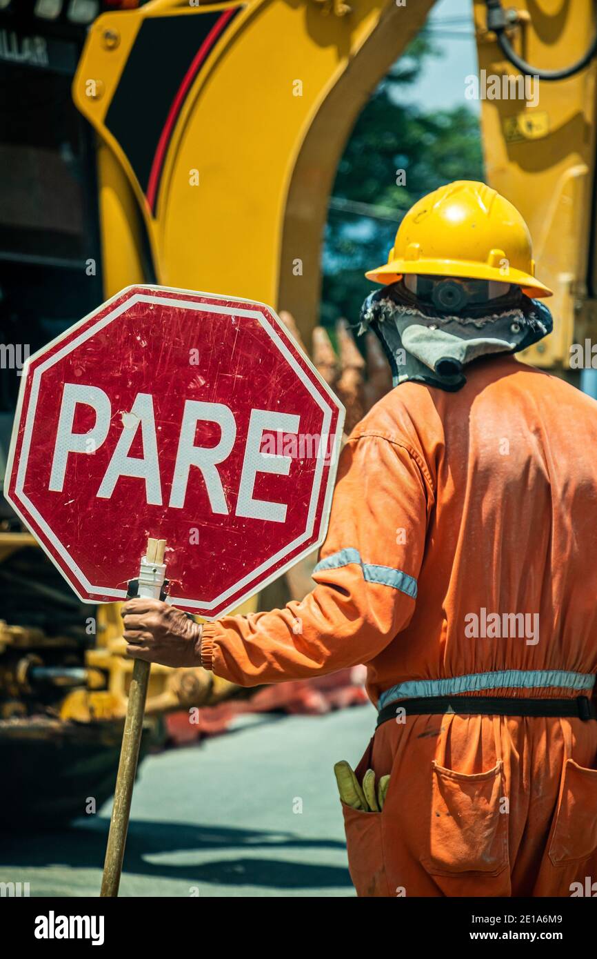 Un uomo sta tenendo un segnale di stop al luogo di costruzione, per avvertire le persone che transitano vicino Foto Stock