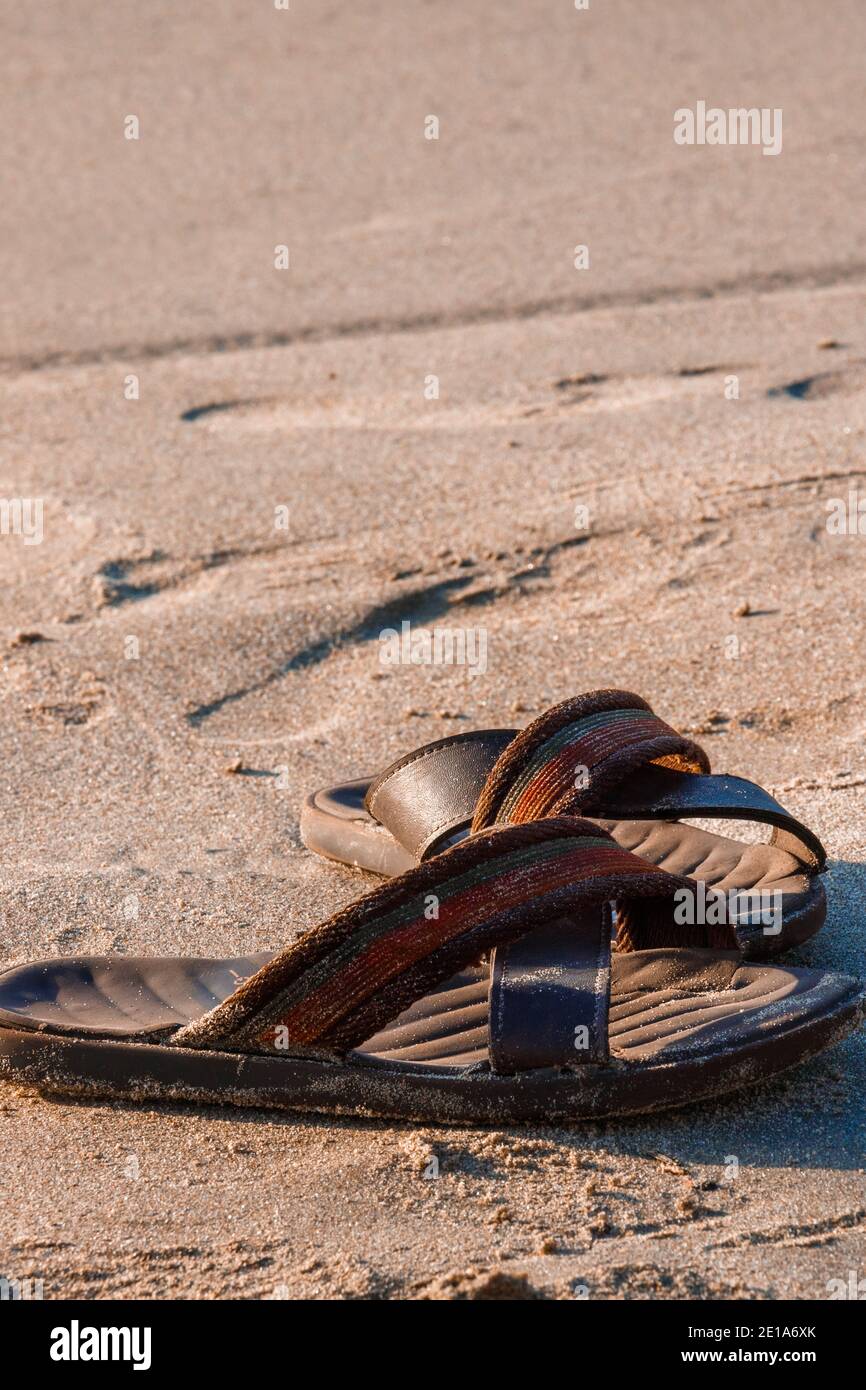 Un paio di sandali o infradito lasciati dal suo proprietario viaggiatore sulla spiaggia di sabbia, mentre fare un tuffo sulle acque tranquille della spiaggia solitaria, questo è il kinf Foto Stock