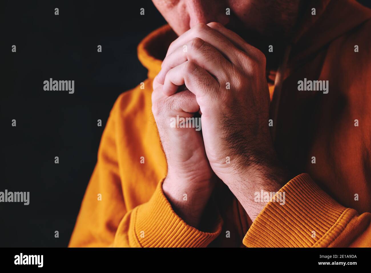 L'uomo cristiano che prega a Dio in camera oscura con mani aggrappate, primo piano con fuoco selettivo Foto Stock
