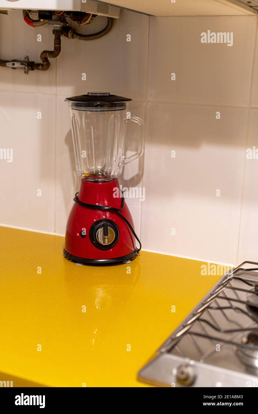 Il mixer elettronico rosso si trova su un tavolo giallo vicino a. piano cottura in cucina Foto Stock