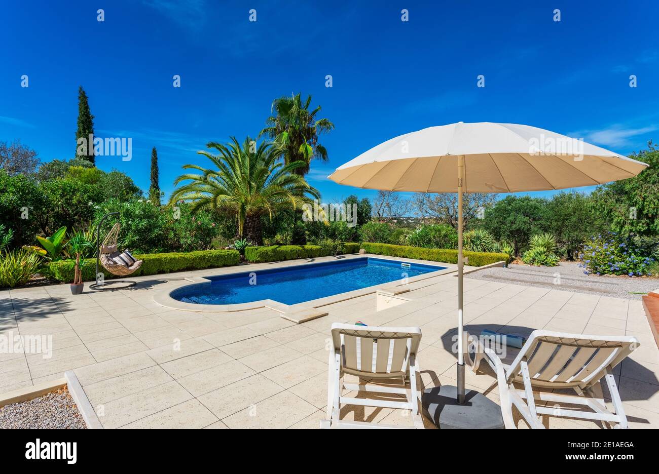Piscina con ombrellone a bordo piscina e lettini. Cielo azzurro e splendidi alberi sullo sfondo in una bella giornata estiva. Foto Stock