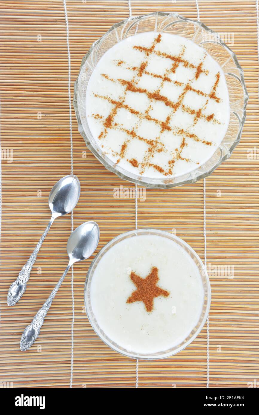 Budino di riso cremoso alla cannella e cucchiai sul tappetino di paglia di bambù come sfondo Foto Stock