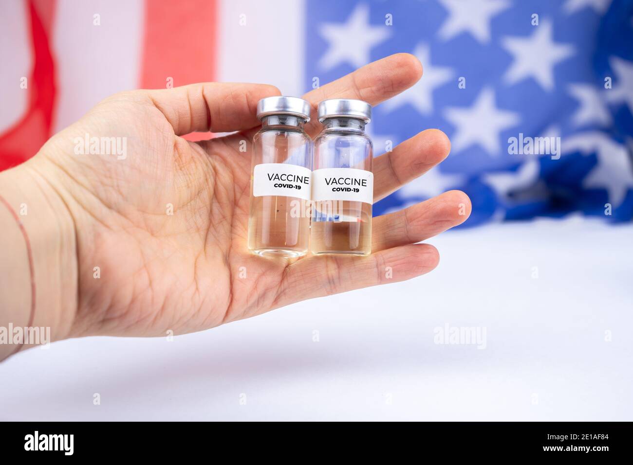 Due flaconi con vaccino covid-19 in una mano. Bandiera DEGLI STATI UNITI sullo sfondo Foto Stock