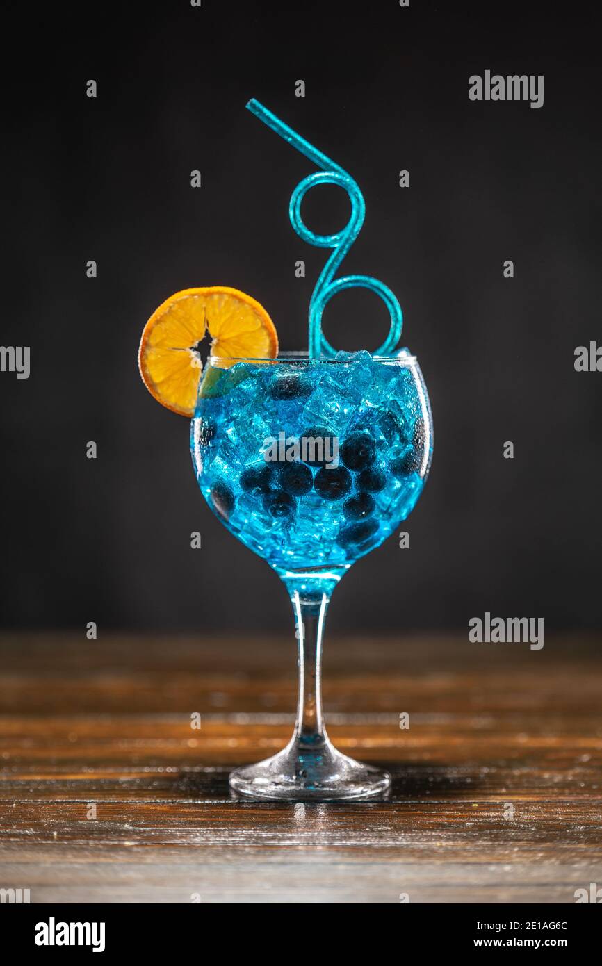 Cocktail blu con mirtillo, fetta di arancia e ghiaccio in un bicchiere su un tavolo di legno Foto Stock