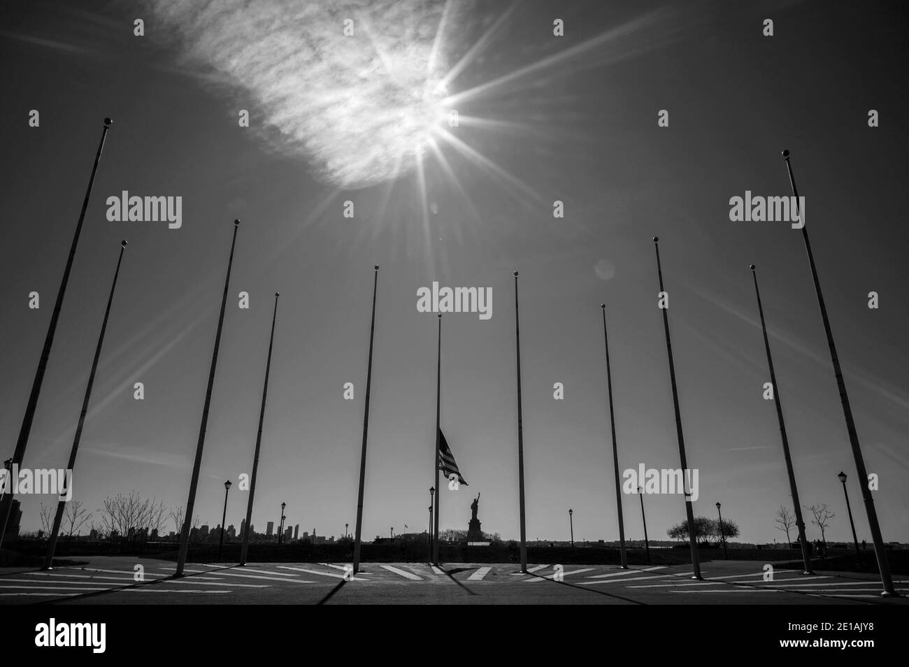 Lonely Lady Liberty guarda NYC circondato da pali di bandiera vuoti e un Liberty state Park vuoto durante la pandemia del coronavirus del 2020. Foto Bnw. Foto Stock