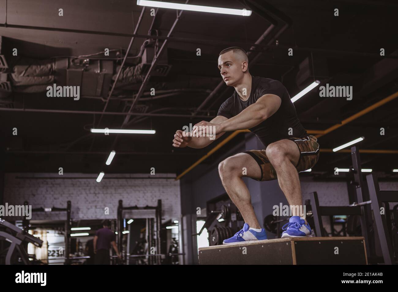 Tiro a tutta lunghezza ad angolo di un atleta crossfit maschile che salta in palestra. Attraente sportivo che si esercita in studio sportivo, saltando o Foto Stock