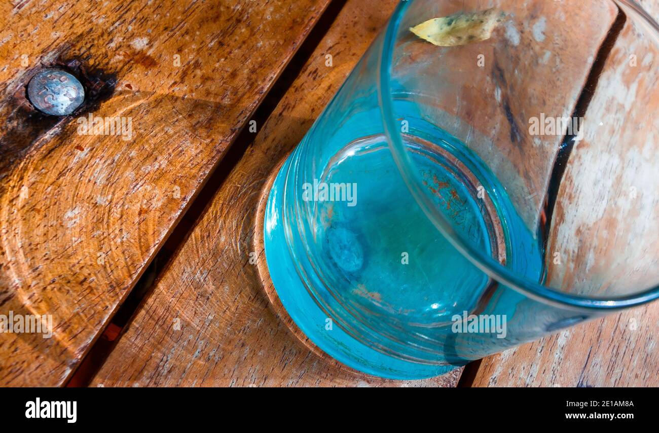 Particolare estremo di un bicchiere d'acqua su un legno rustico tabella che crea alcune caustiche e ombre Foto Stock