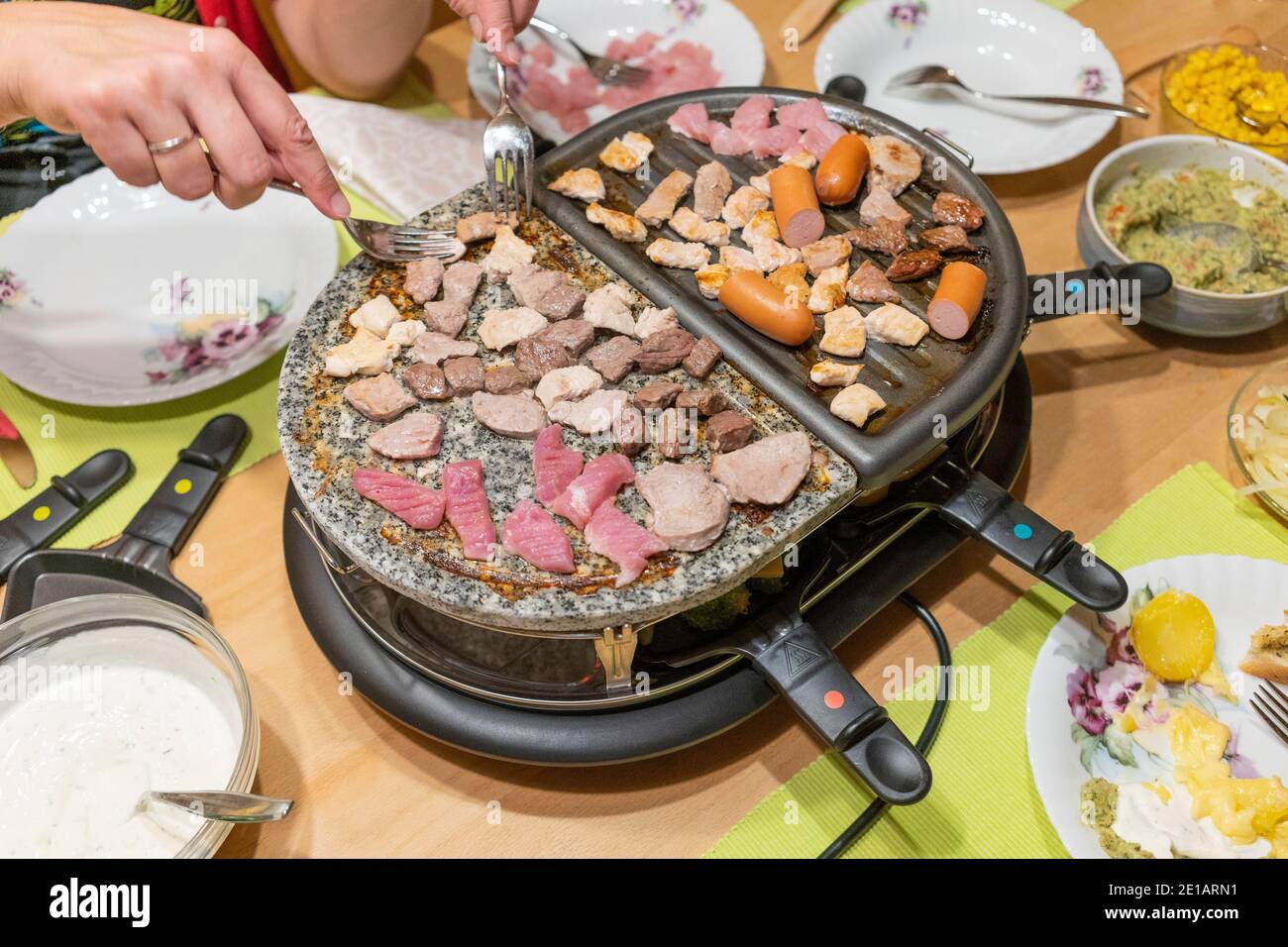 Grigliate di carne e cottura del formaggio in padelle elettriche griglia per raclette da tavolo al centro di un tavolo su Festa di Capodanno in Austria Foto Stock