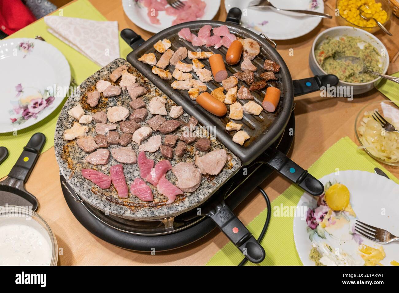 Grigliate di carne e cottura del formaggio in padelle elettriche griglia per raclette da tavolo al centro di un tavolo su Festa di Capodanno in Austria Foto Stock