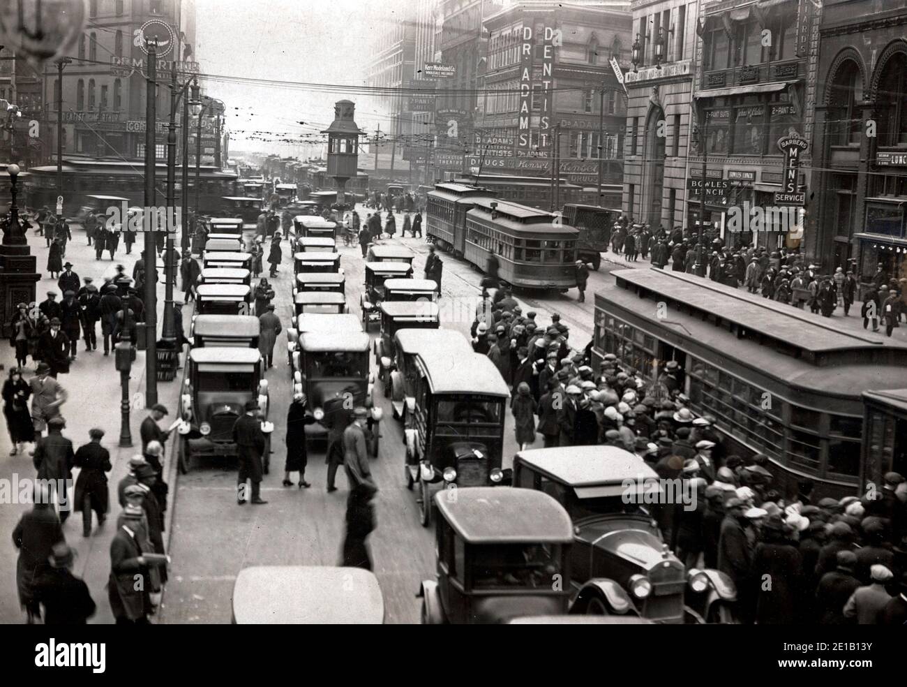 Angolo tra Michigan e Griswold. Molto traffico in auto, un grande gruppo di persone che salite a bordo di un tram. Grandi edifici commerciali sullo sfondo. Torre del traffico nel mezzo della strada, con una persona in piedi, circa 1920 Foto Stock