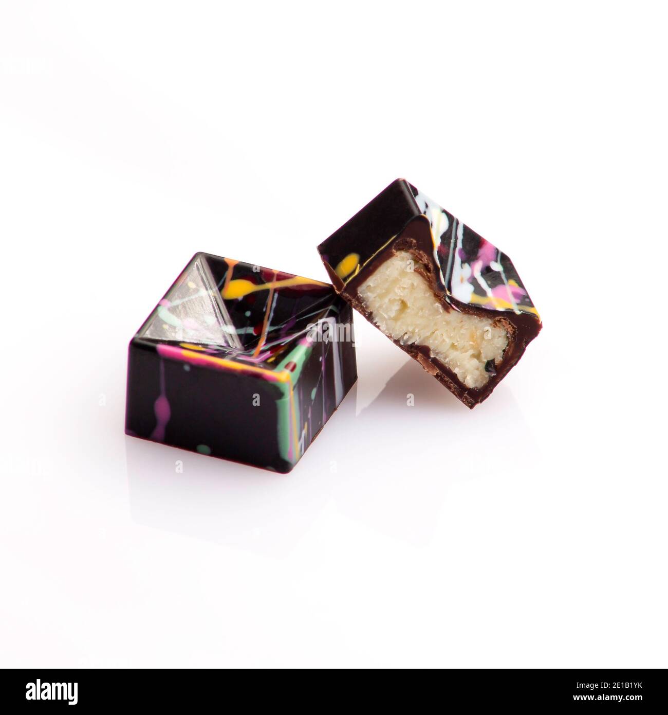 bomboni dolci fatti a mano di cioccolato di lusso a forma geometrica ripieni di cocco ganache decorate con colorata arte astratta su sfondo bianco Foto Stock