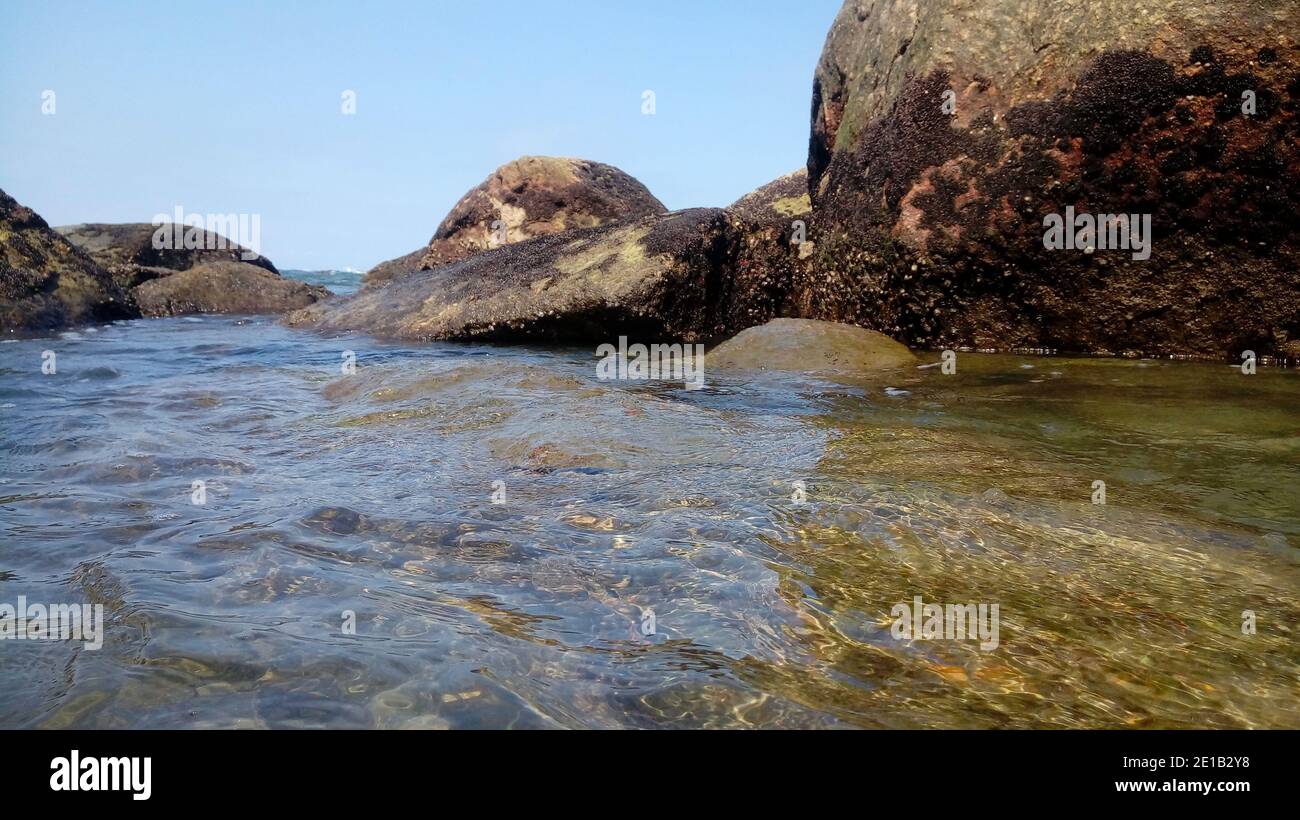 Piscina naturale circondata da rocce vicino all'oceano in un giorno di sole luminoso Foto Stock