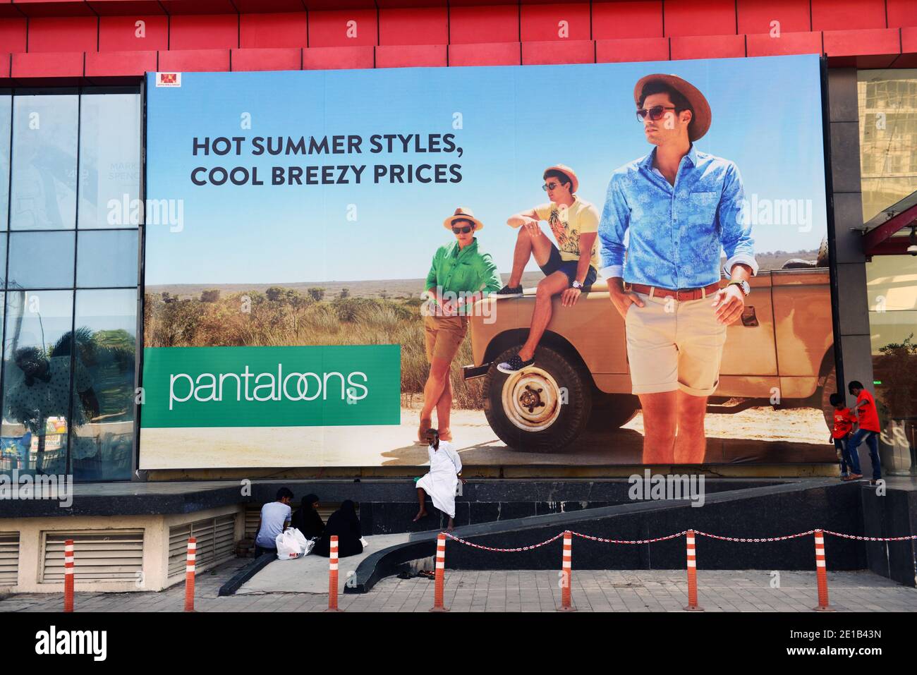 Un uomo indiano seduto da una grande pubblicità. Foto Stock