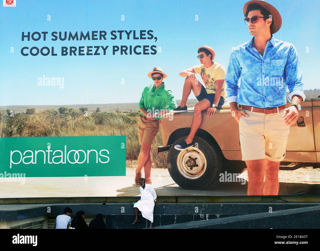 Un uomo indiano seduto da una grande pubblicità. Foto Stock