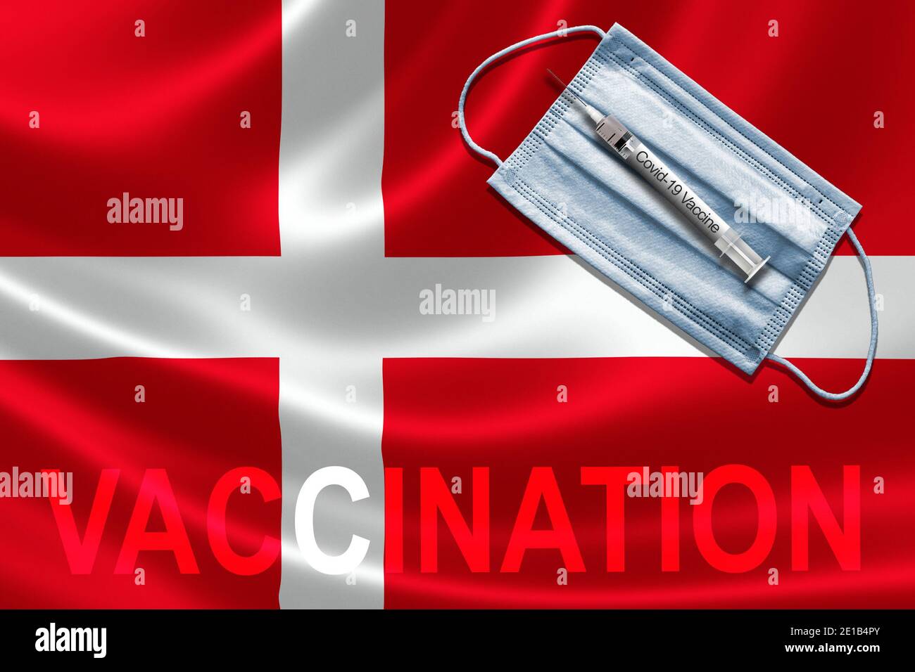 COVID-19 vaccinazione in Danimarca Concept con maschera facciale e siringa di vaccino ad ago sulla bandiera danese. Foto Stock