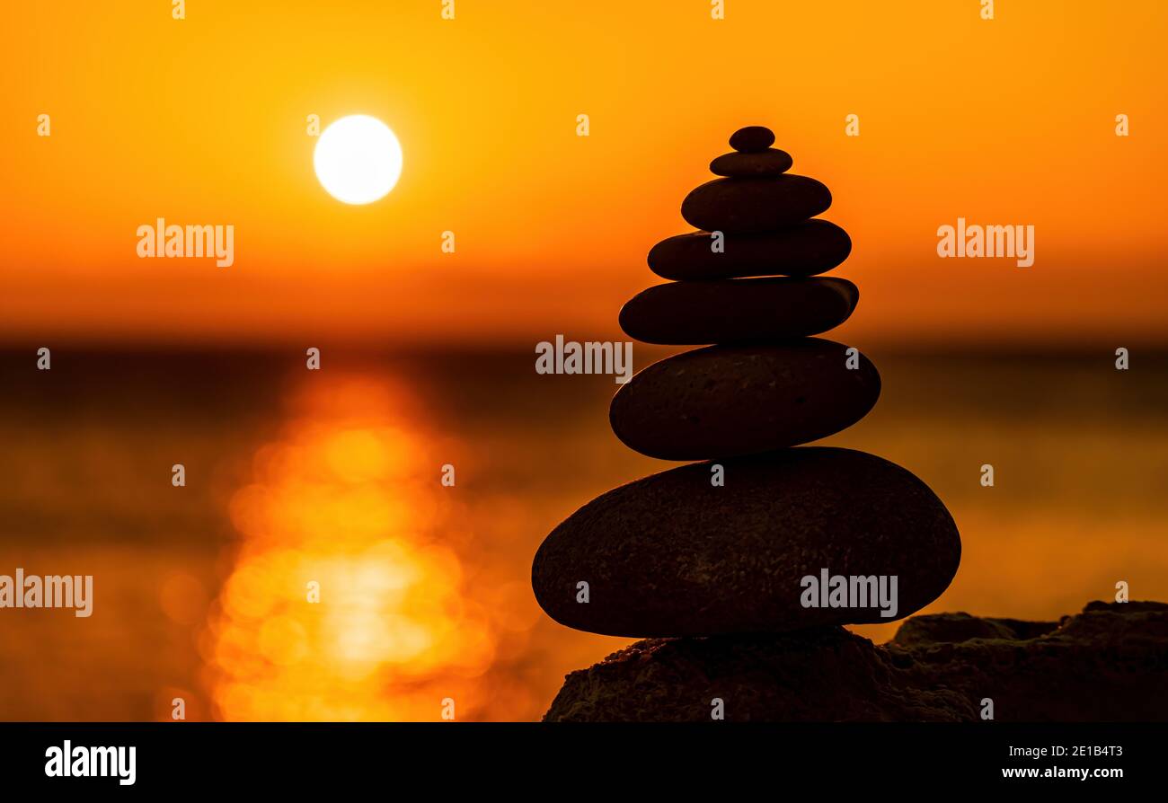 Profilo a piramide di ciottoli bilanciato sulla spiaggia. Astratto caldo tramonto bokeh con Mare sullo sfondo. Pietre Zen sulla spiaggia di mare, meditazione, spa Foto Stock